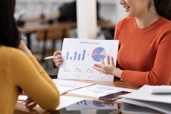 Two business women sit at desk discuss project details business valuation